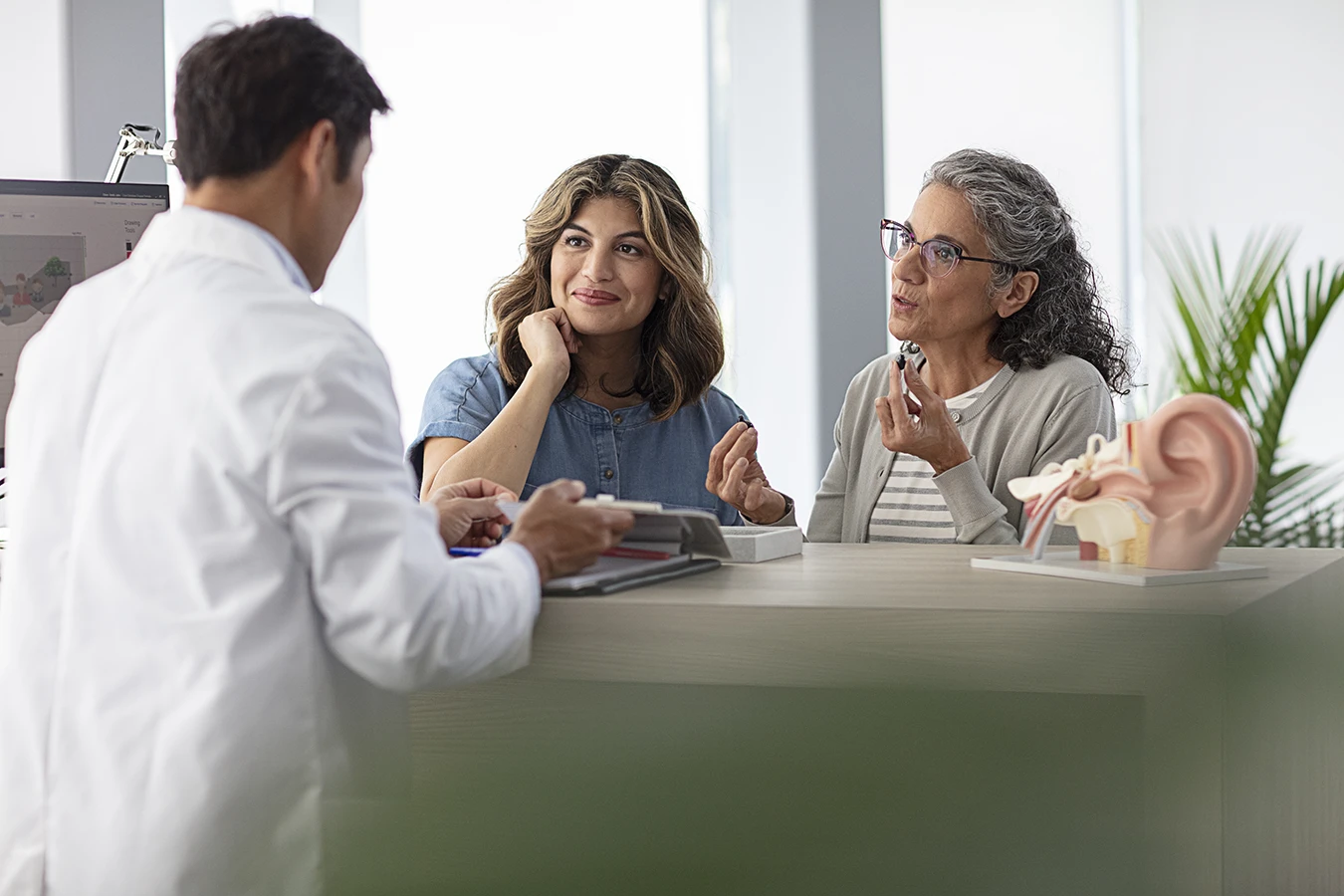 An older adult women, and her middle aged daughter talking with a hearing care specialist about hearing aids
