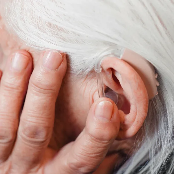 Closeup senior woman holding hand up to ear to keep hearing aid in her ear.