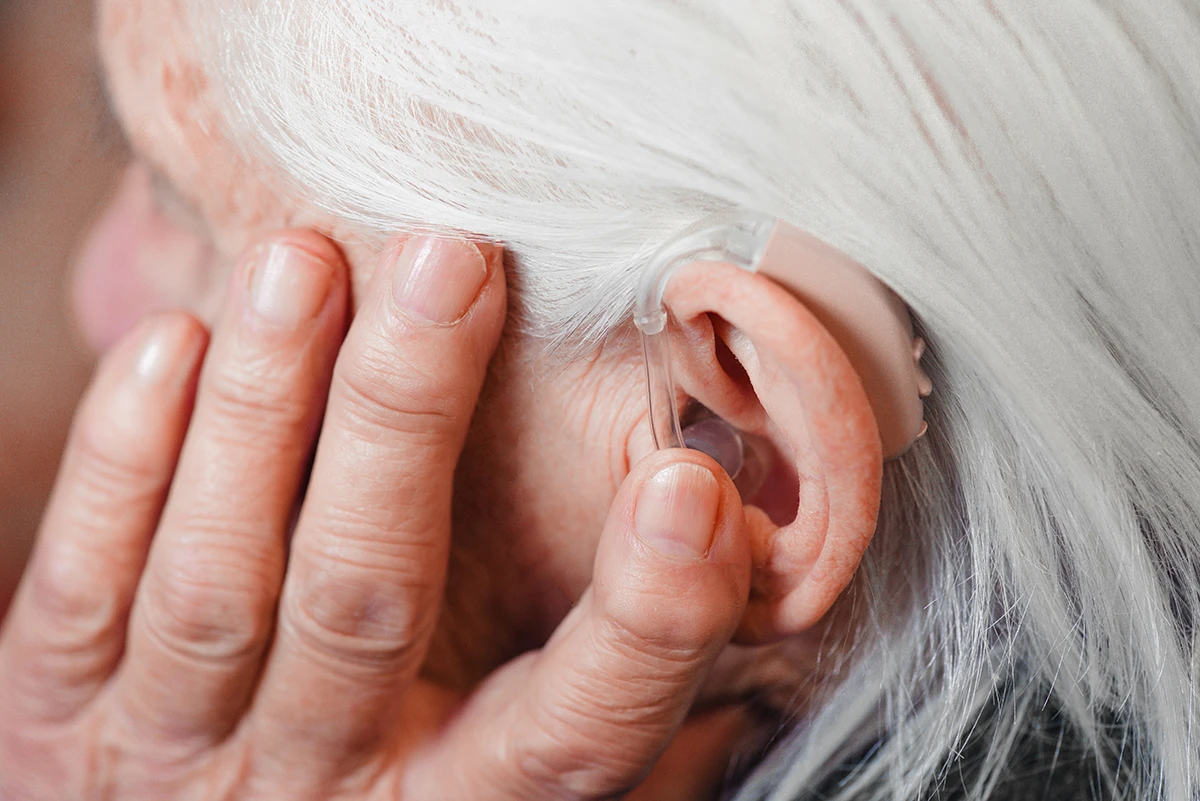 Closeup senior woman holding hand up to ear to keep hearing aid in her ear.