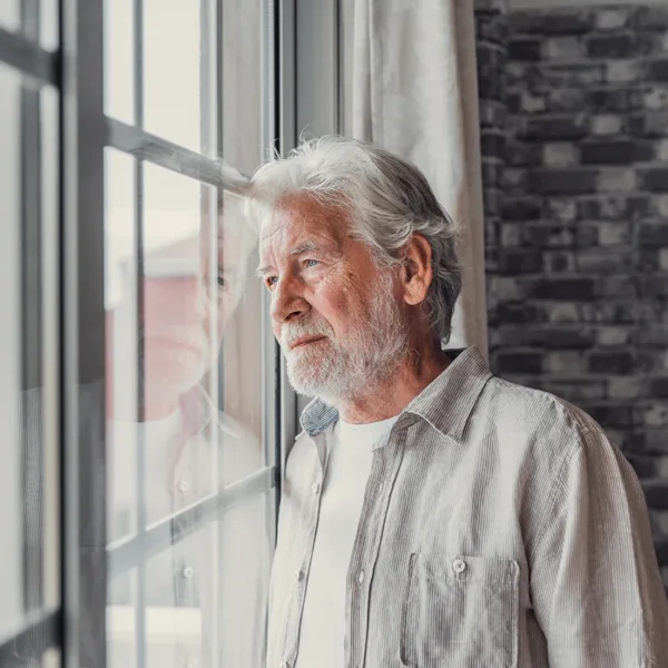 A mature, senior man, who appears to be sad, lonely, or depressed, looking in distance out of window, symbolizing the potential emotional impact of hearing loss.