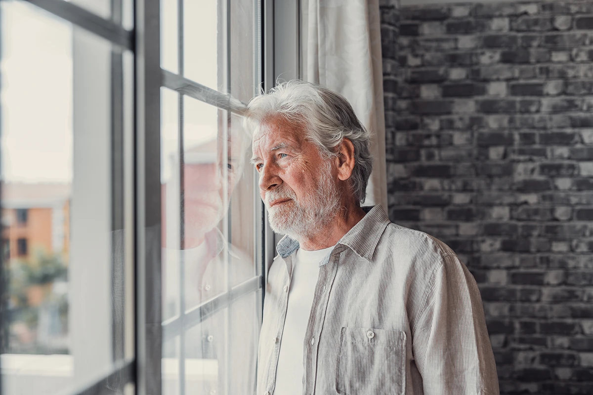 A mature, senior man, who appears to be sad, lonely, or depressed, looking in distance out of window, symbolizing the potential emotional impact of hearing loss.