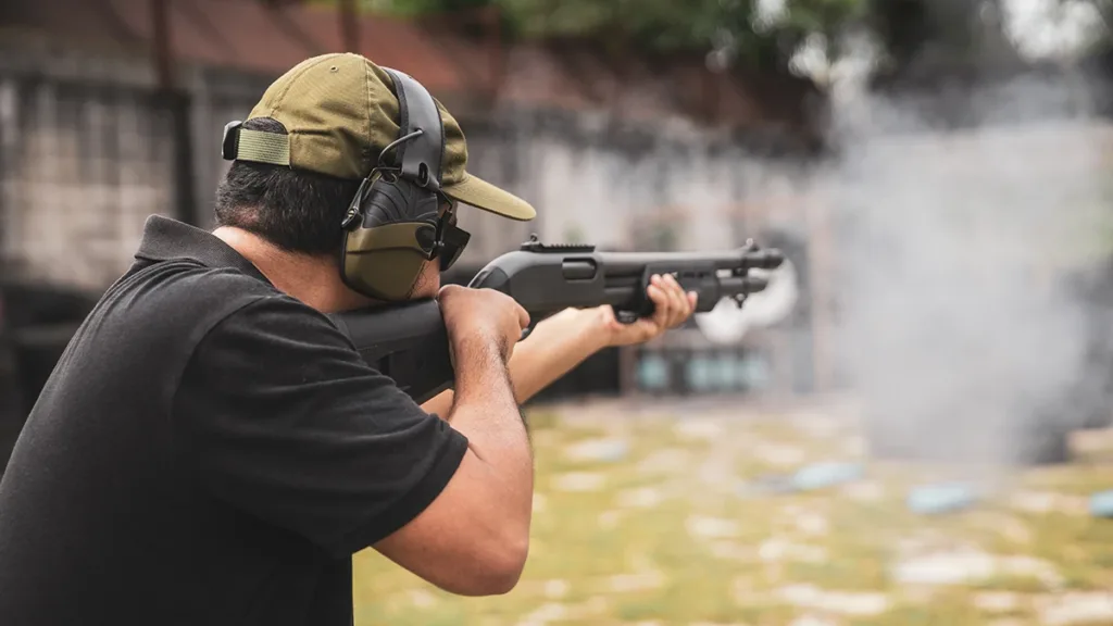 A man at an outdoor shooting range wearing NRR hearing protection ear muffs while target shooting