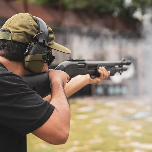 A man at an outdoor shooting range wearing NRR hearing protection ear muffs while target shooting