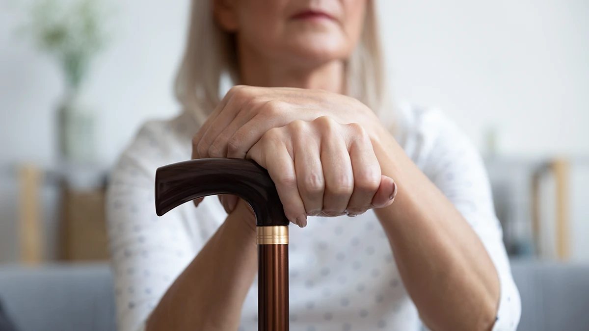 An older aged women sitting down holding a cane due to the physical effects of hearing loss causing issues with balance, dizziness, and vertigo