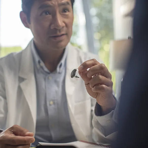 A behind-the-ear BTE hearing aid being held up by a hearing care specialist who is slightly out of focus in the background