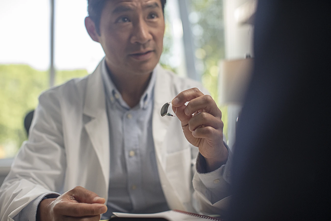 A behind-the-ear BTE hearing aid being held up by a hearing care specialist who is slightly out of focus in the background