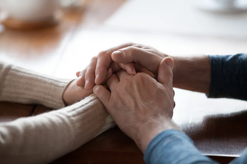close up of senior, retirement age, older couple holding hands in a caring gesture to console one another, symbolizing how hearing loss can impact close relationships.