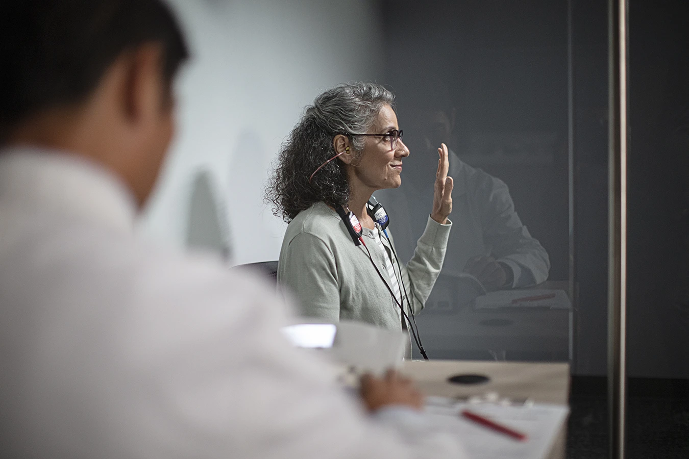A woman sitting in a soundproof both with her hand raised as she takes a hearing test during a hearing aid consultation at a hearing clinic
