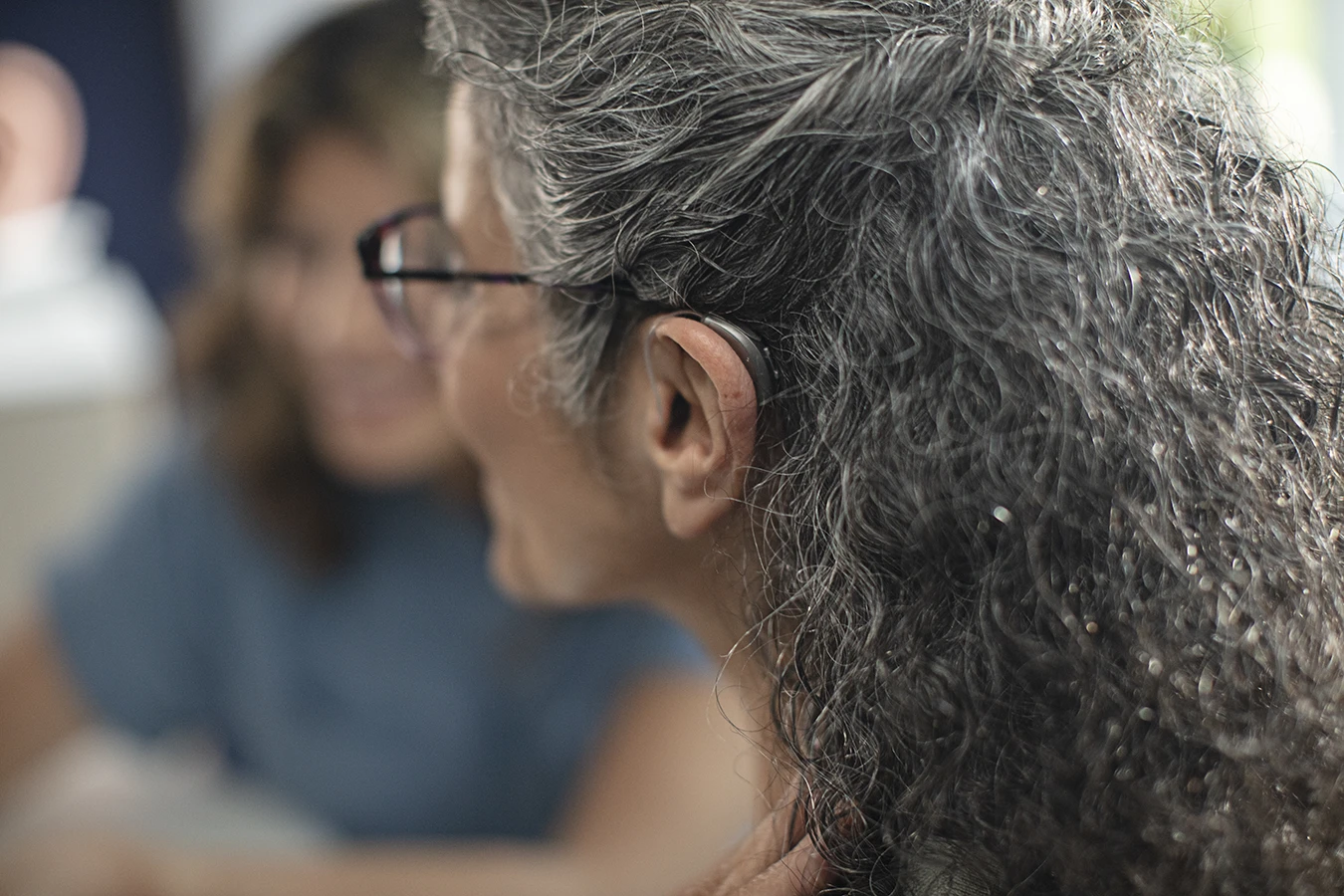 The side profile of a woman in an a hearing clinic during a hearing aid consultation, wearing a Bluetooth hearing aid