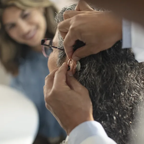 The side profile of a woman in an a hearing clinic during a hearing aid consultation, as her hearing care specialists fits a new hearing aids in her ear and powers it on