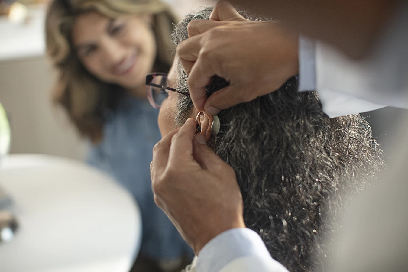 The side profile of a woman in an a hearing clinic during a hearing aid consultation, as her hearing care specialists fits a new hearing aids in her ear and powers it on