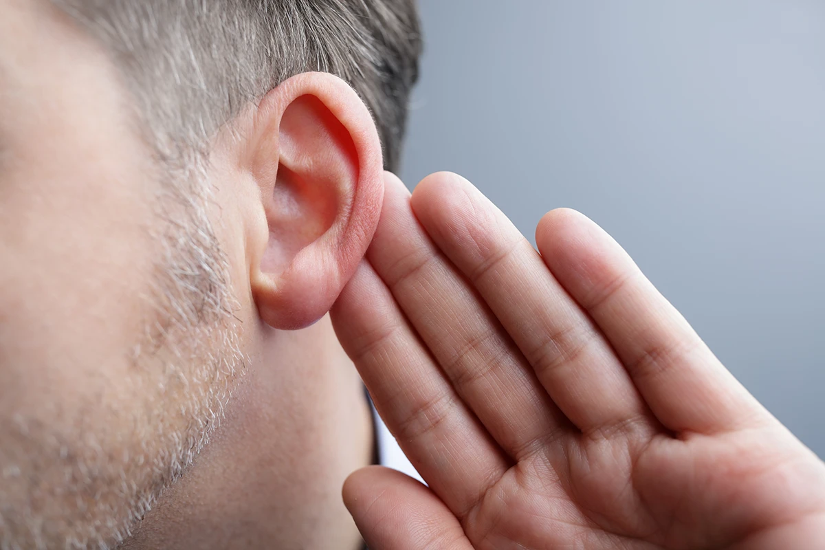 Older man holding had up to his ear indicating he is trying to hear something more clearly, age-related hearing loss symptoms