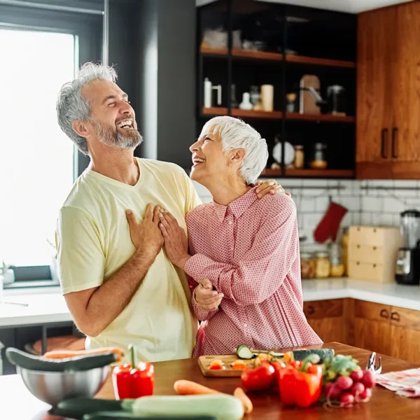 Older woman and man, married couple, happily preparing food together in the kitchen, cooking a healthy meal together.