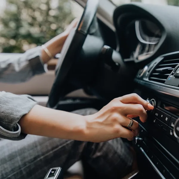 close up of woman's hands turning up the volume on her car stereo, symbolizing a hearing loss risk