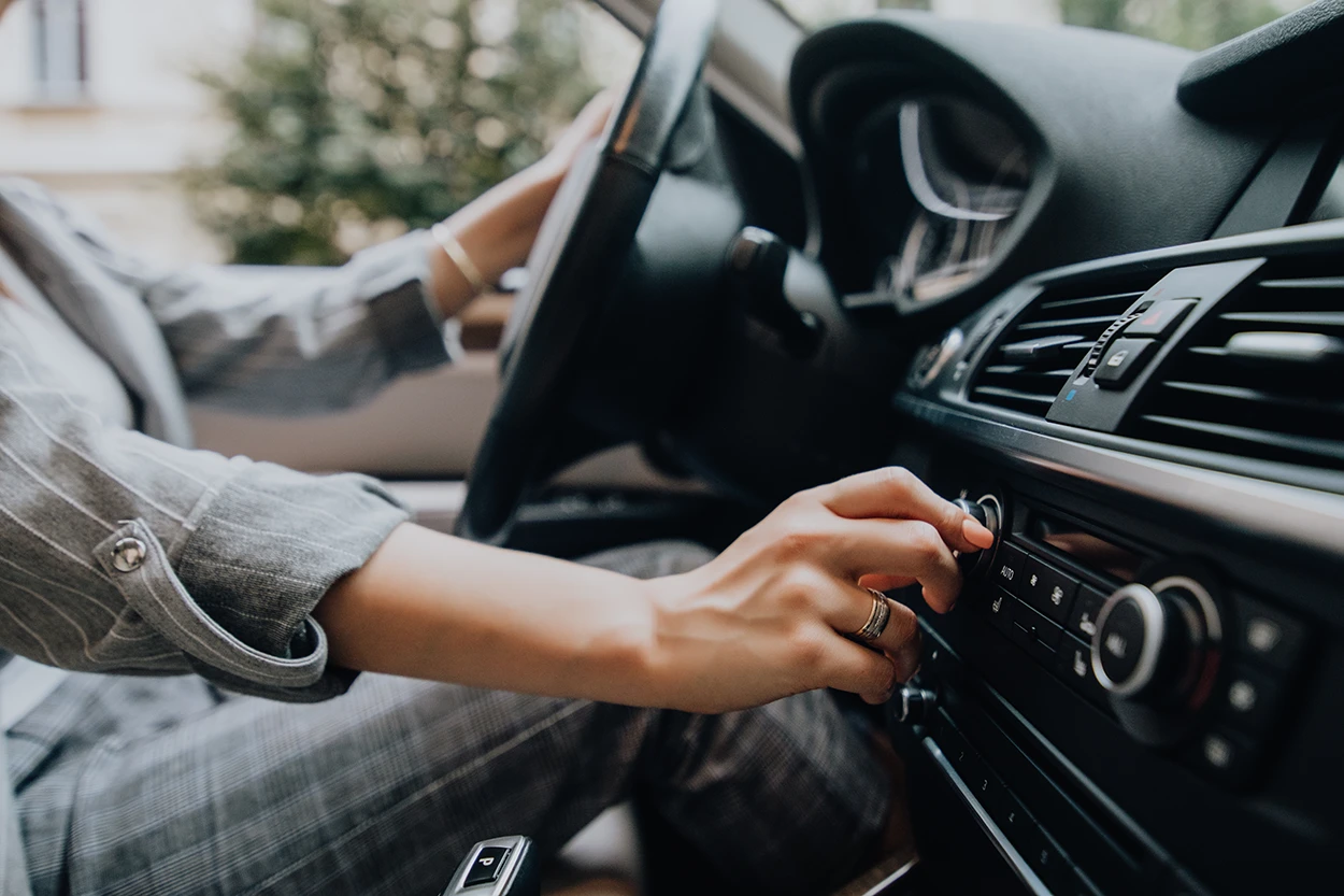 close up of woman's hands turning up the volume on her car stereo, symbolizing a hearing loss risk