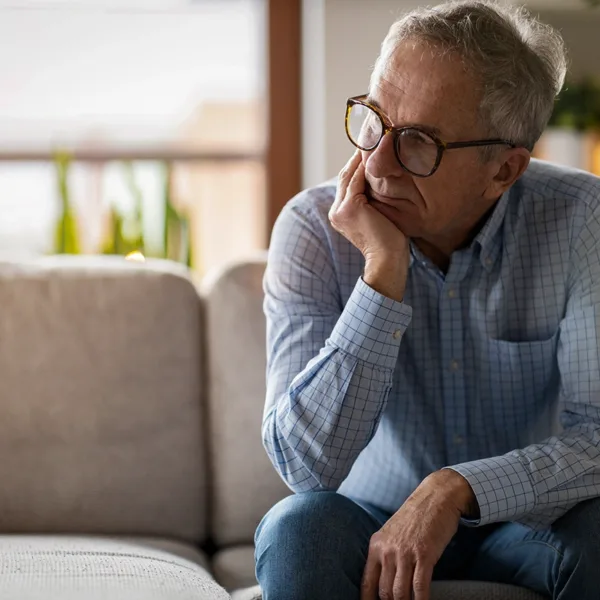 A senior man sitting alone in his home looking worried, sad, and tired due to listening fatigue from untreated hearing loss.