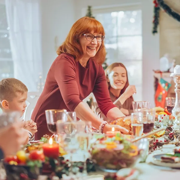 Large family of multiple generations smiling, talking, and laughing, as they sit around the dinner table with holiday decorations in the background, symbolizing happy holiday gatherings with hearingloss