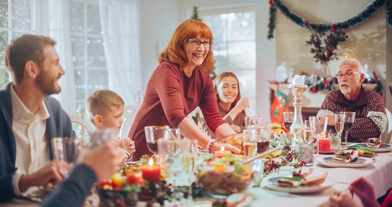 Large family of multiple generations smiling, talking, and laughing, as they sit around the dinner table with holiday decorations in the background, symbolizing happy holiday gatherings with hearingloss