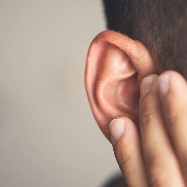 Close up of the side of a man's head, holding his hand up to his ear indicating ear pain from an ear infection