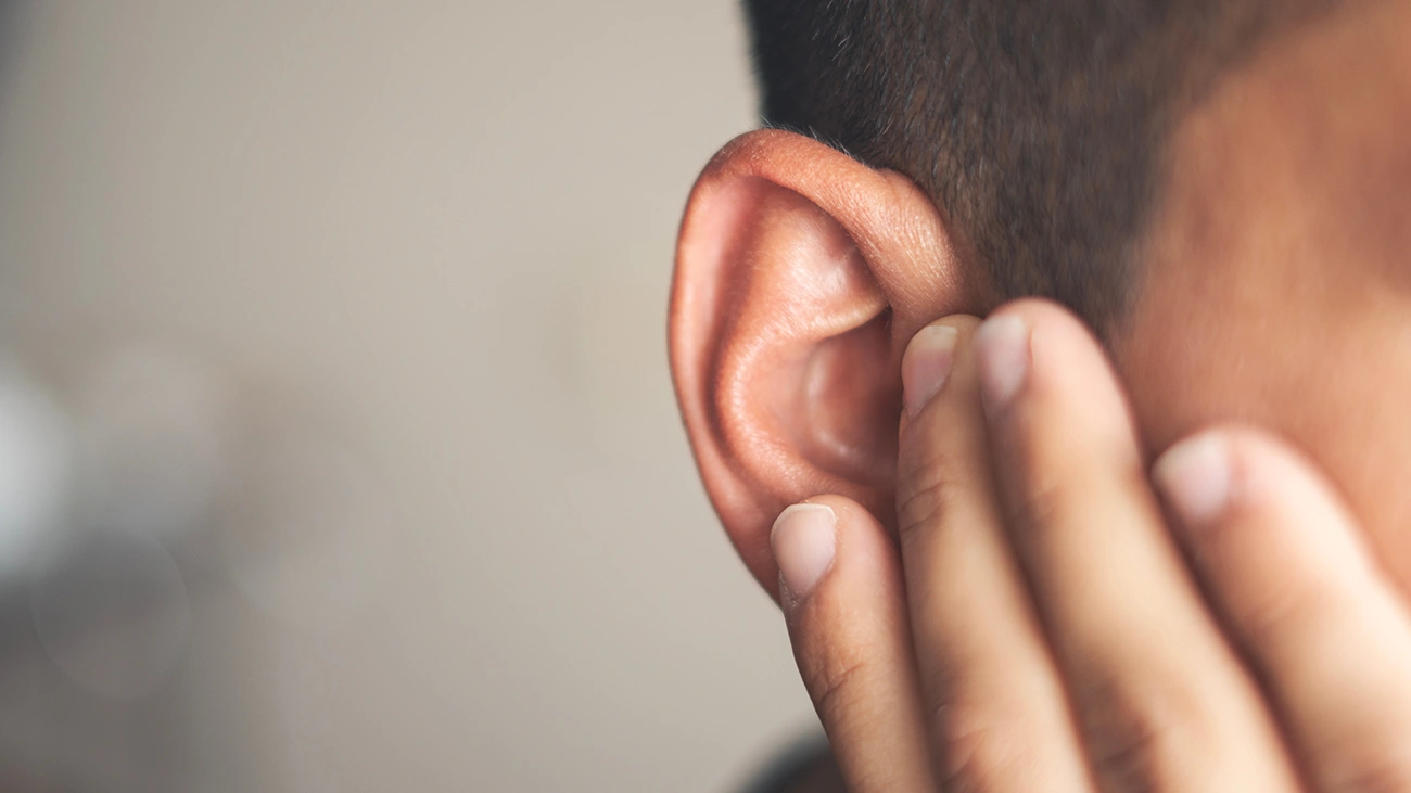 Close up of the side of a man's head, holding his hand up to his ear indicating ear pain from an ear infection
