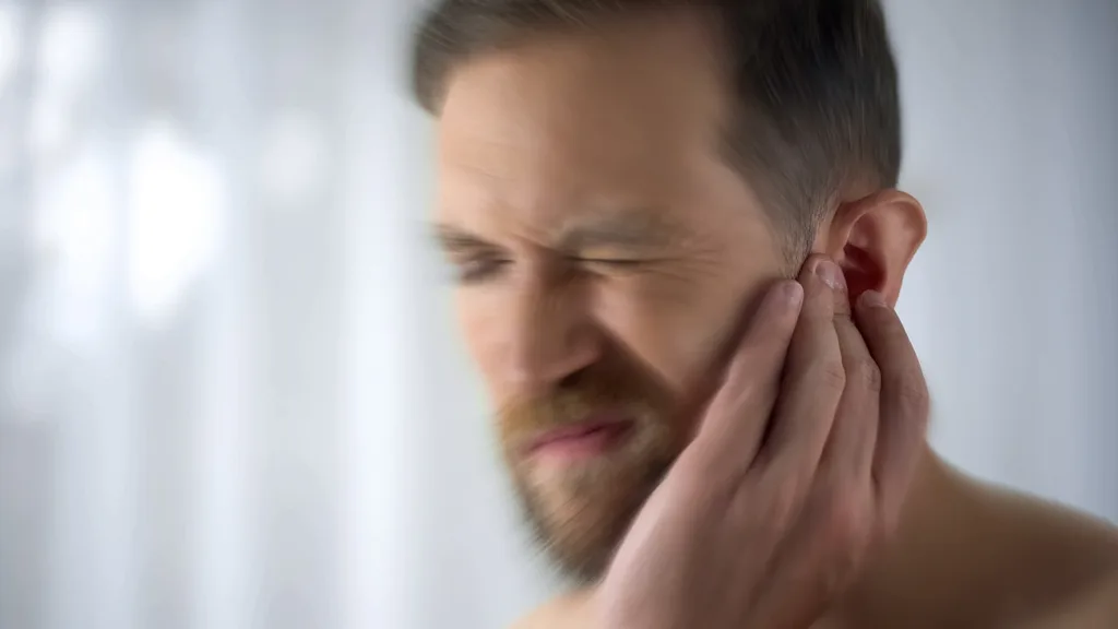 close up of middle aged man wincing and hold ear as he experiences paint in his middle ear causes by an ear infection