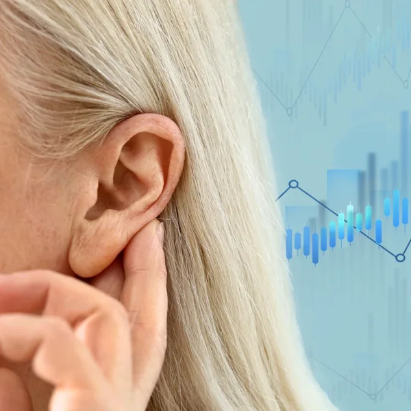 The side profile of a woman holding her hand up to her ear as if to help her hear better, with statistic graphics out of focus in the background, showing the concept of hearing loss statistics in the United States