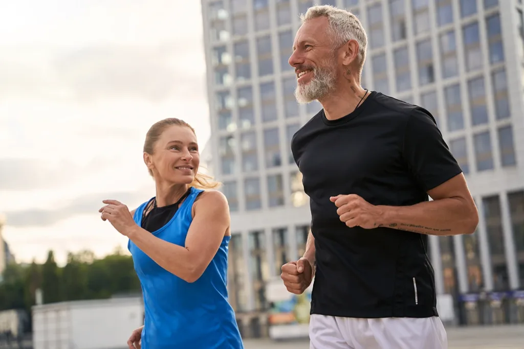 Active middle aged couple, man and woman in sportswear looking happy while jogging together outdoors. Symbolizes the latest hearing aid technology and health and wellness feature integration