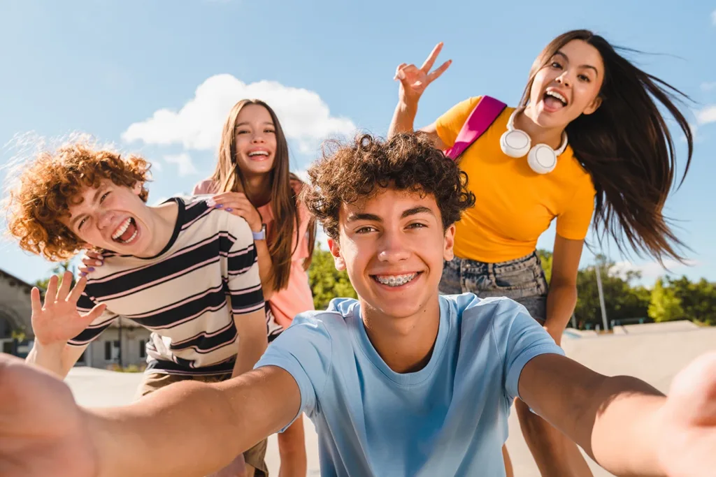 Four teenagers at school, during lunch break, taking a selfie together in the quad