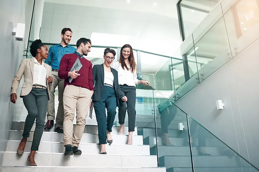 A group of professional adult colleagues talking together while walking down stairs in a large modern office
