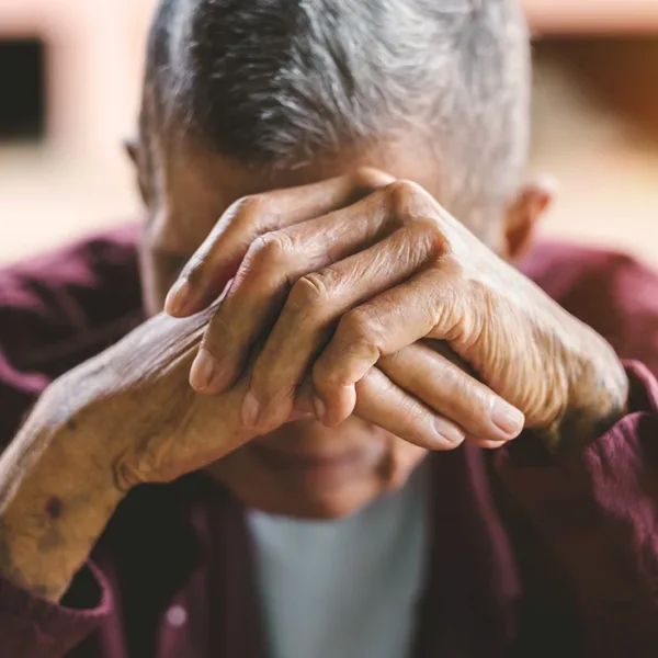 A senior man covering his face as he looks down in sadness, symbolizing the risk of loneliness and/or cognitive decline in older adults with untreated hearing loss