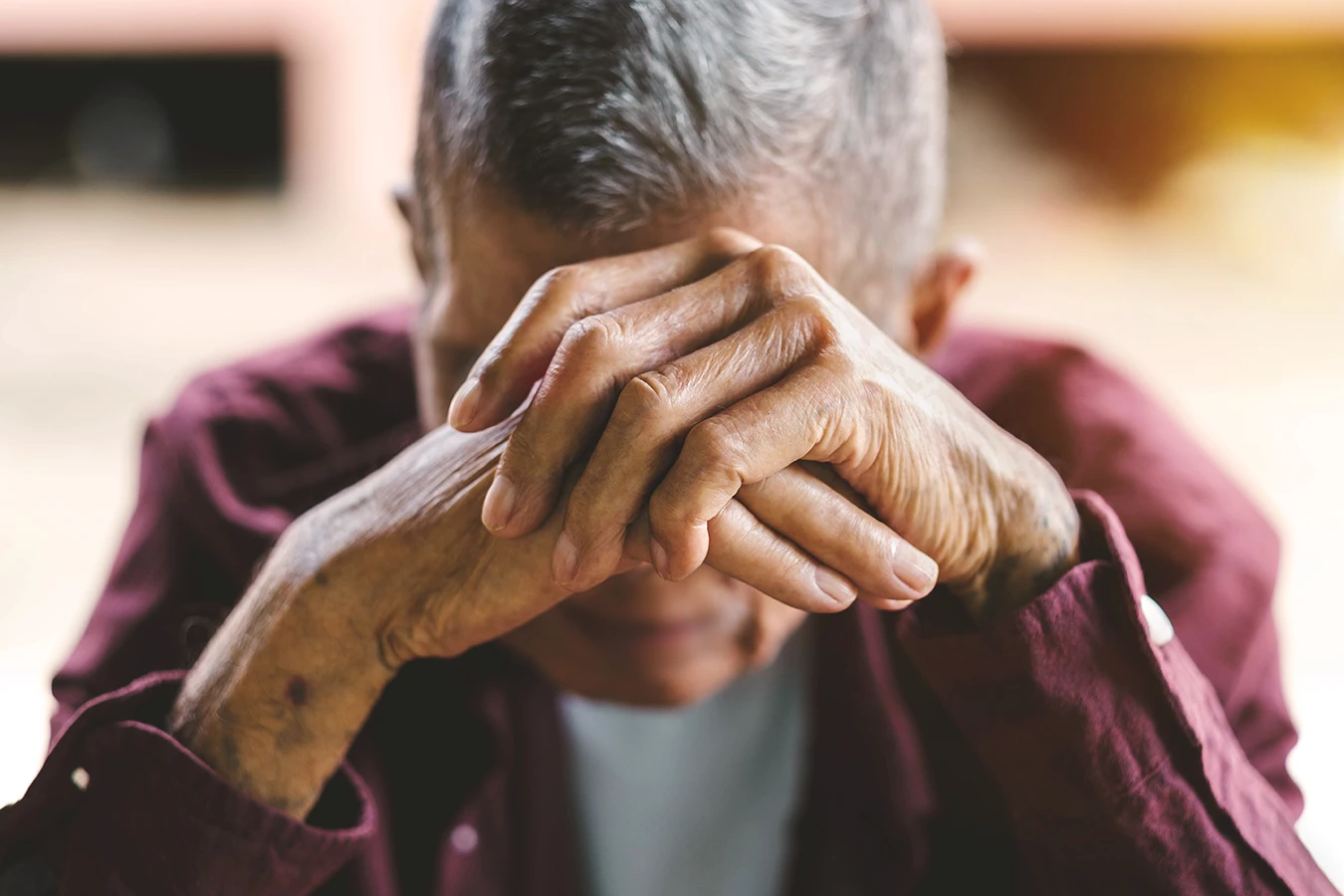 A senior man covering his face as he looks down in sadness, symbolizing the risk of loneliness and/or cognitive decline in older adults with untreated hearing loss