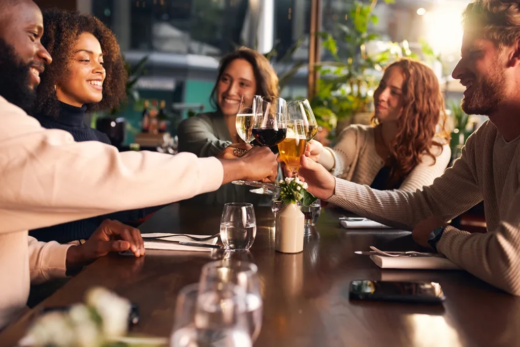 A group of five young adults, men and women, at a wine bar cheersing glasses of wine 