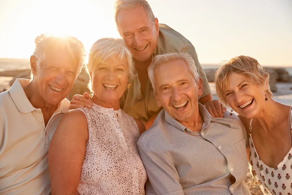 What hearing loss looks like for the Baby Boomer Generation concept: five older adult, baby boomer, men and women, smiling and looking at the camera while taking a selfie.