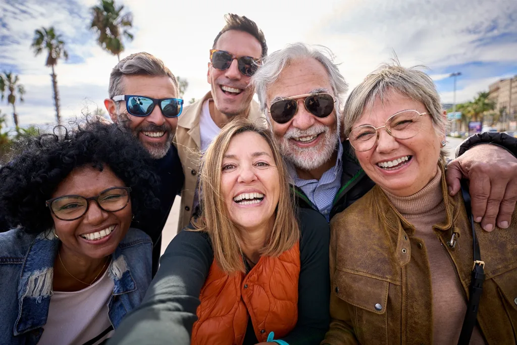 What hearing loss looks like for Gen X concept: six middle aged adults, Gen X, men and women, smiling and looking at the camera while taking a selfie.