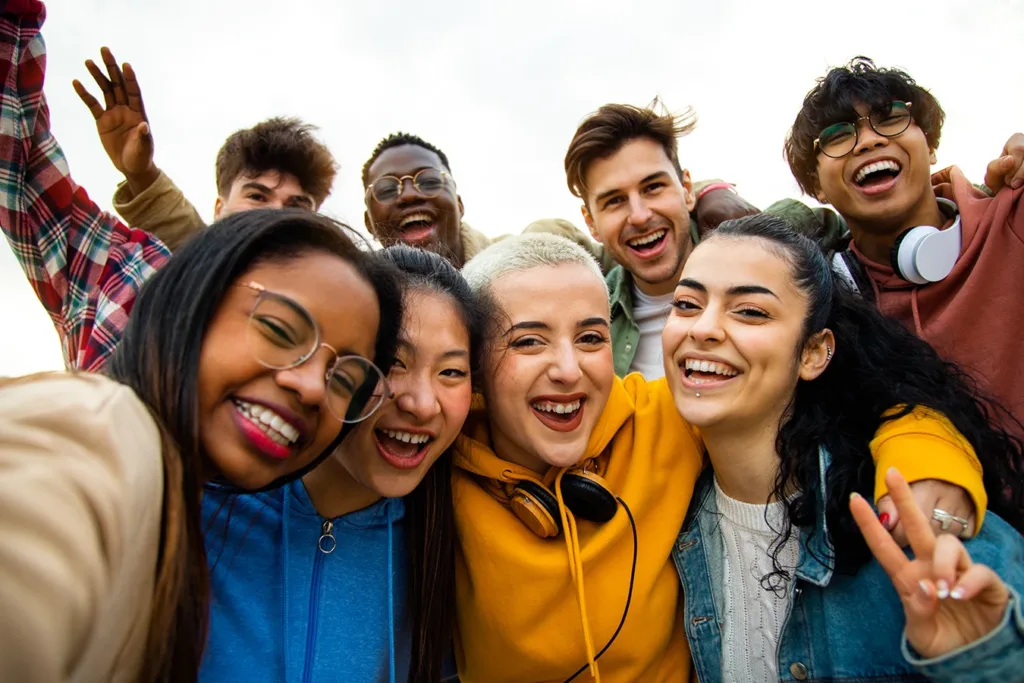 What hearing loss looks like for Gen Z concept: eight young adults, Gen Z, men and women, smiling and looking at the camera while taking a selfie.
