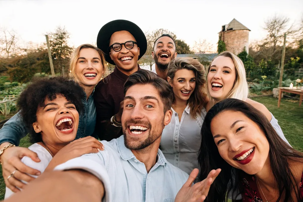 What hearing loss looks like for the Millennial Generation concept: eight adults, Millennials, men and women, smiling and looking at the camera while taking a selfie.