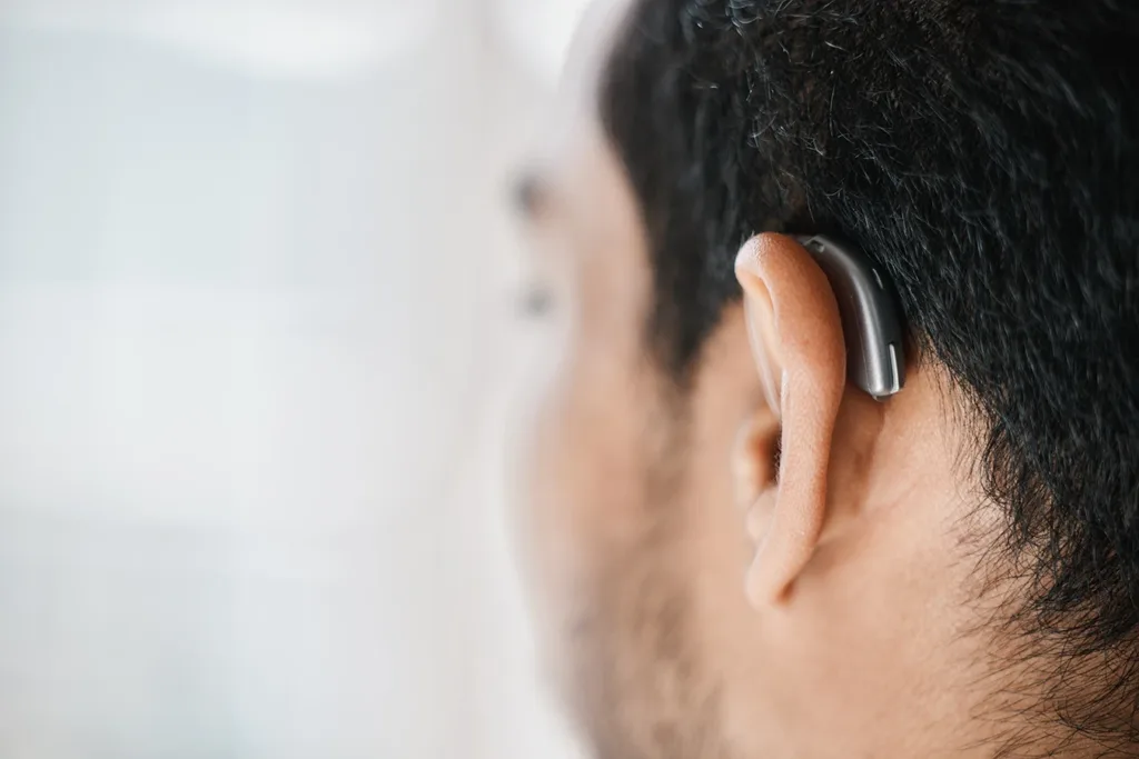 A close up of the side profile on a man with short dark hair wearing a very small and discreet behind-the-ear (BTE) hearing aid.