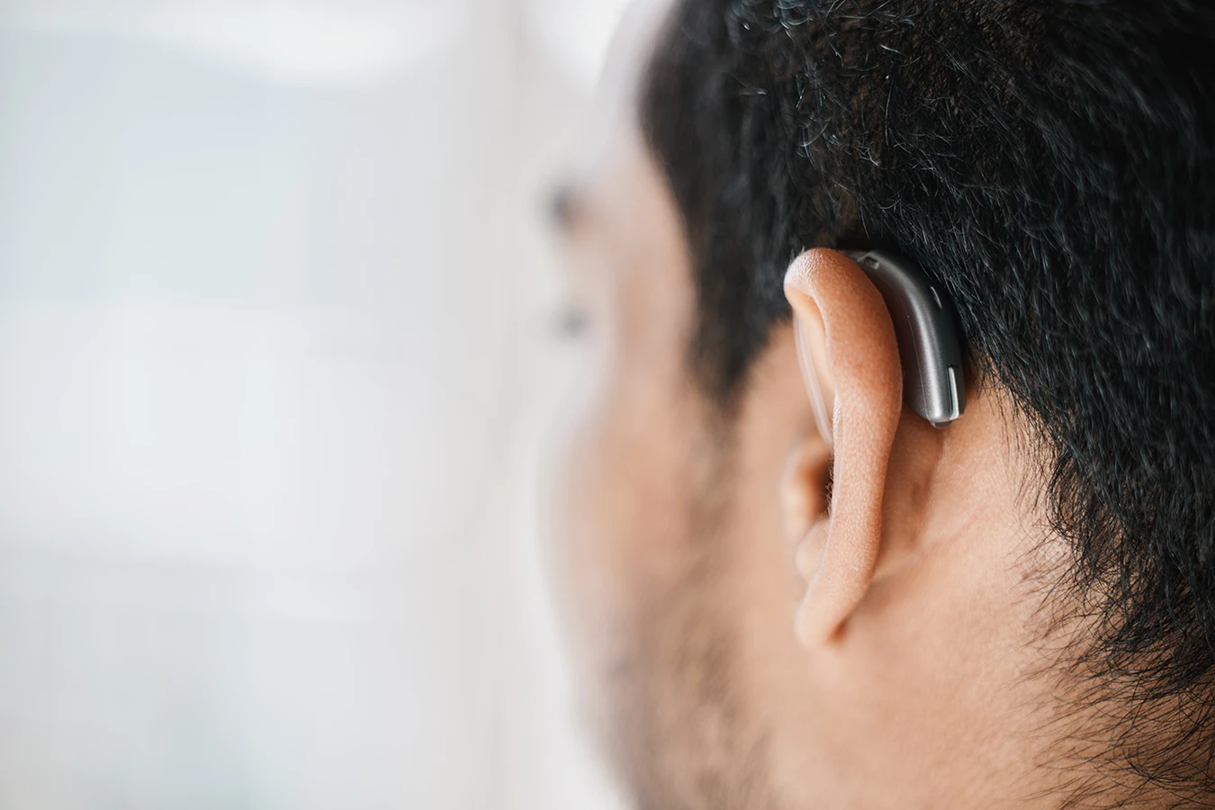 A close up of the side profile on a man with short dark hair wearing a very small and discreet behind-the-ear (BTE) hearing aid.