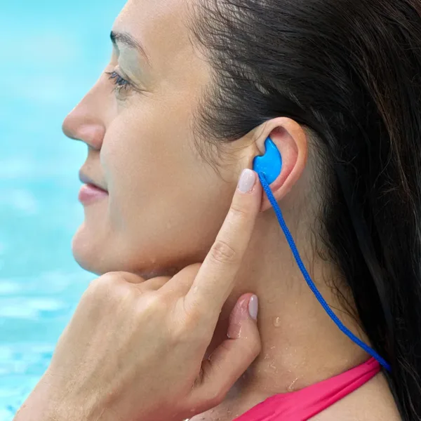 Side profile of a middle aged women with long dark hair, standing in a swimming pool, putting earplugs in to prevent swimmer's ear