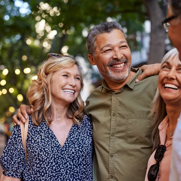 A group of four older adults, outdoors at an street fair, farmers market, community event, enjoying time together as a friend group, representing how hearing aids combat loneliness in older adults.