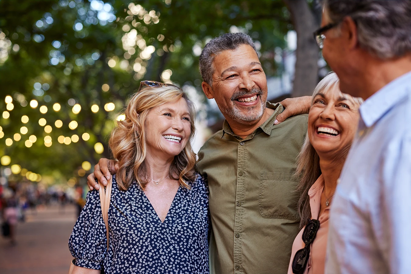 A group of four older adults, outdoors at an street fair, farmers market, community event, enjoying time together as a friend group, representing how hearing aids combat loneliness in older adults.