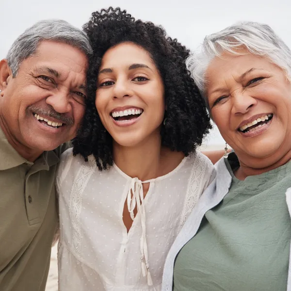 A selfie-style portrait of a young women with her older aged parents at the beach, smiling, and laughing, enjoying quality time together, symbolizing helping a loved one adjust to new hearing aids