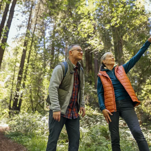 A happy, healthy, and active senior couple, husband and wife, hiking through the Redwood Forest near San Francisco, CA, symbolizing hearing aids safeguarding physical health.