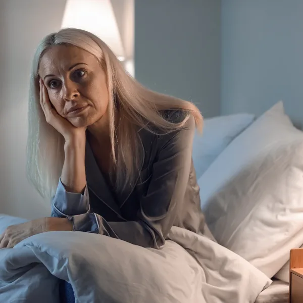Mature woman, sitting up in bed, at night, unable to sleep, insomnia, demonstrating how hearing loss can impact sleep quality