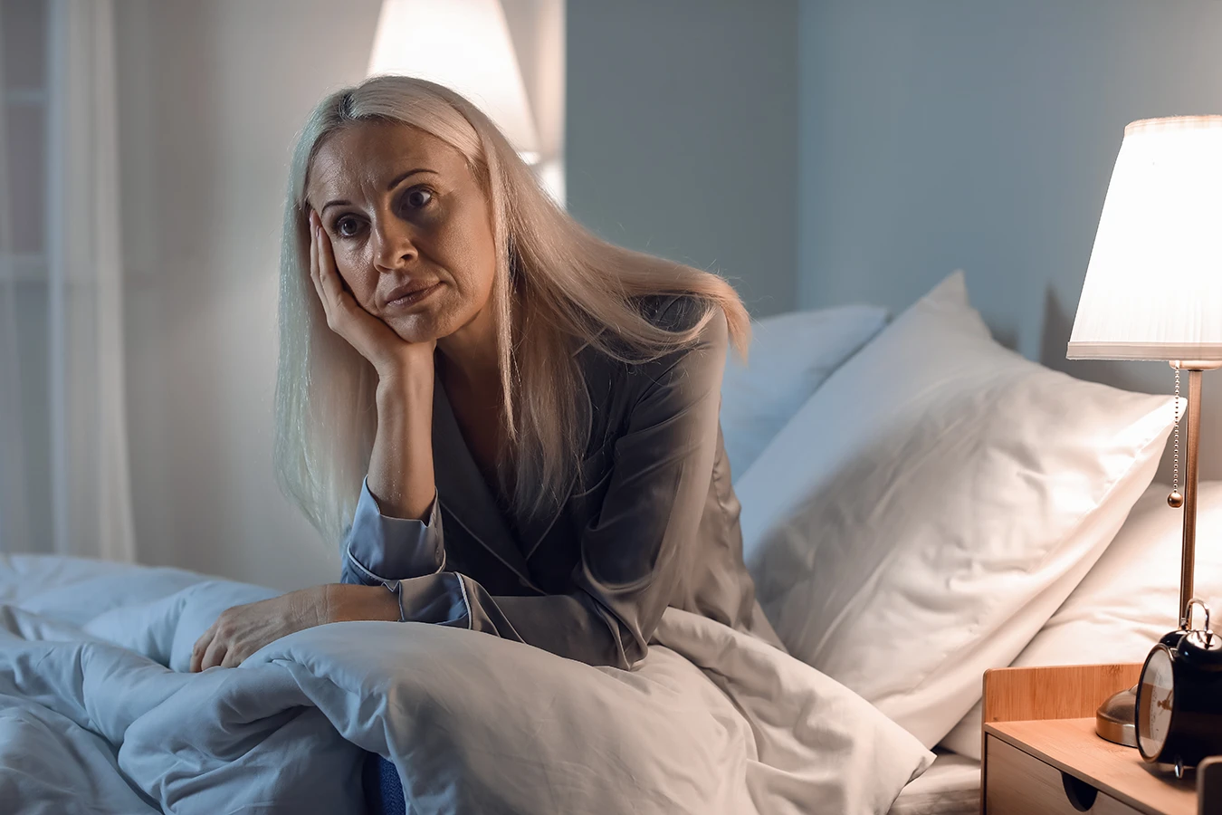 Mature woman, sitting up in bed, at night, unable to sleep, insomnia, demonstrating how hearing loss can impact sleep quality