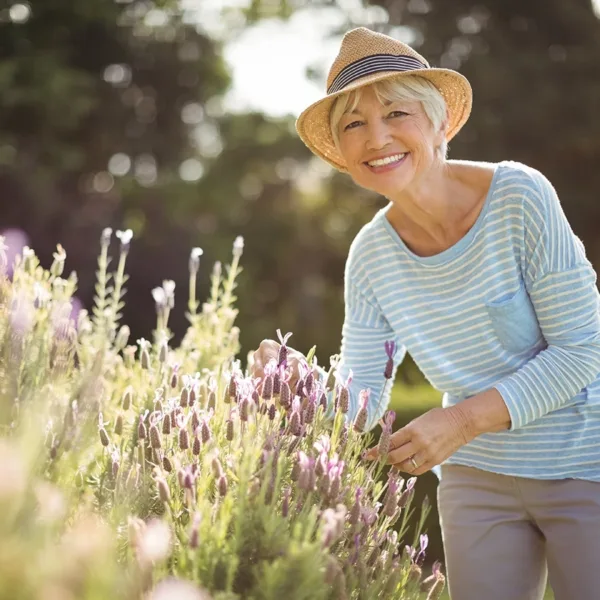 Happy older woman, smiling while tending to her lavender garden in backyard, symbolizing the many ways hearing aid use can benefit the mental health and emotional well-being of older adults.